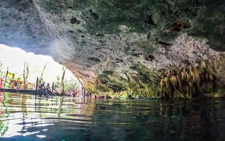 Cenote cave with swimmers exploring the water, part of Akumal sea turtle snorkeling tour.