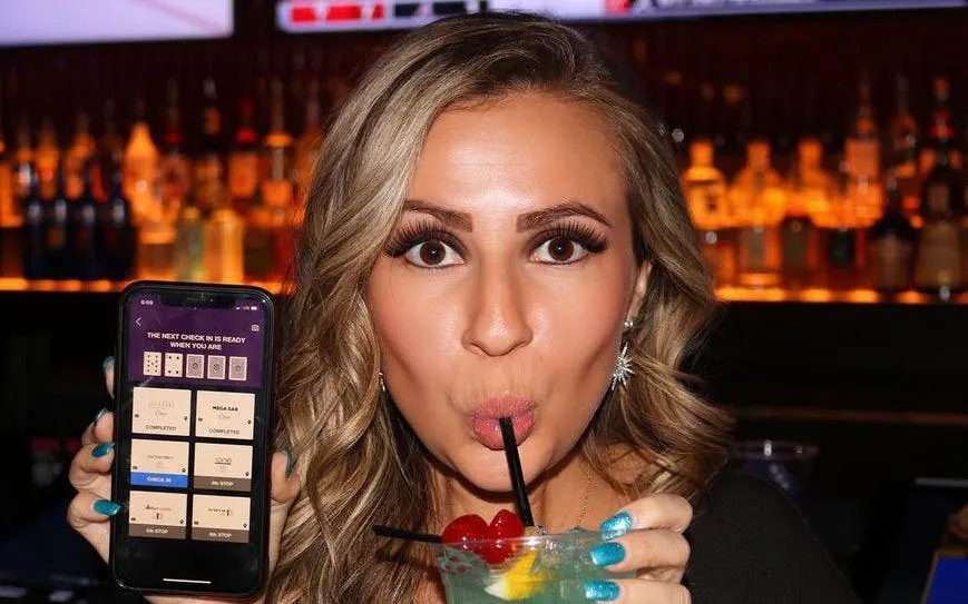 Woman enjoying a cocktail at a bar in Downtown Las Vegas, holding a phone displaying a poker game.