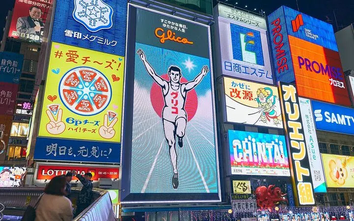 Dotonbori Glico sign illuminated at night in Osaka, Japan, with tourists taking photos.