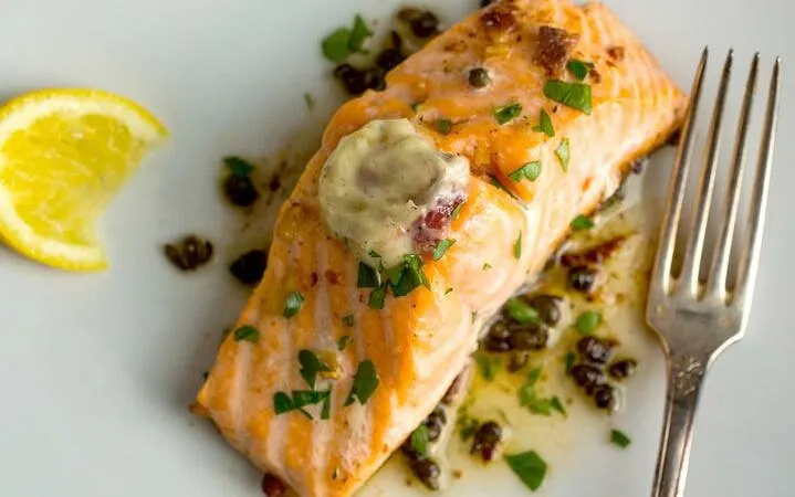 Grilled salmon with herbs and lemon slice on a plate, part of Sapa food tour dinner.