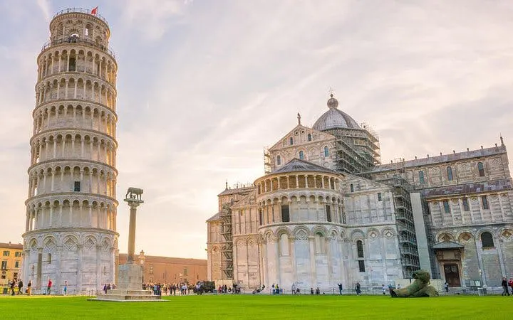 Leaning Tower of Pisa and Pisa Cathedral with tourists on the lawn.