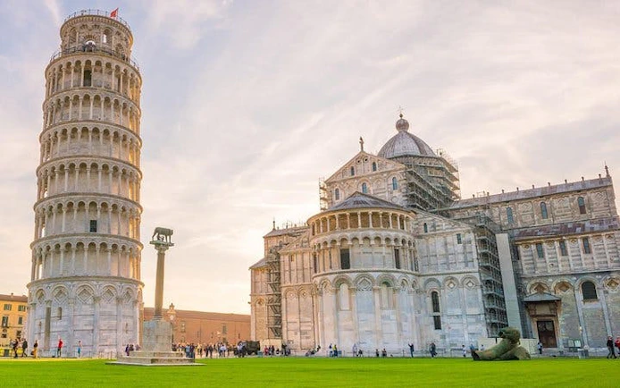 Leaning Tower of Pisa and Pisa Cathedral with tourists on the lawn.
