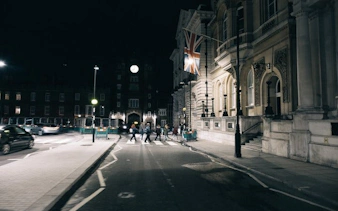 Nighttime canal walk in Little Venice, London, with people crossing a street near historic buildings.
