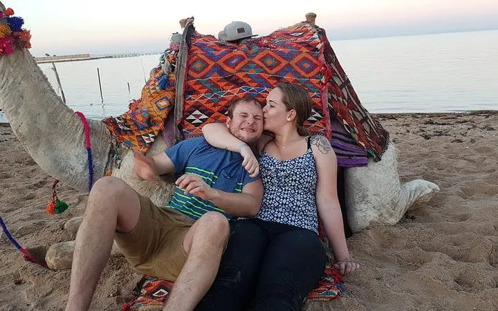 Couple sitting with camel on Sharm El Sheikh beach during sunset.