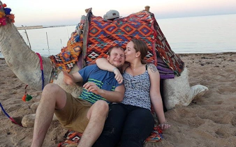 Couple sitting with camel on Sharm El Sheikh beach during sunset.