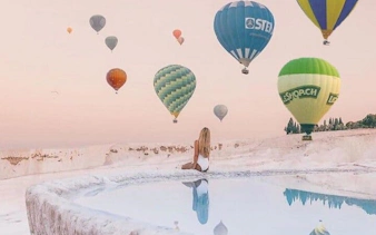 Hot air balloons over Pamukkale travertines with a person sitting by a thermal pool.