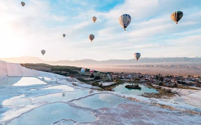 Hot air balloons over Pamukkale travertines and Hierapolis, Turkey, with scenic landscape.