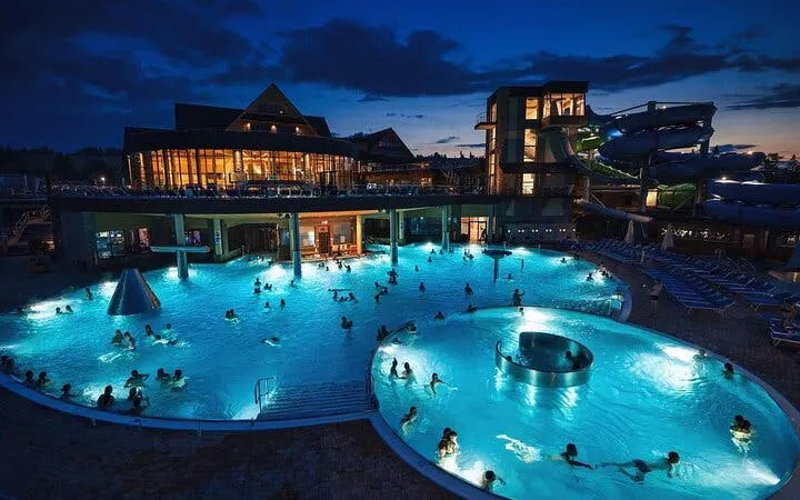 Chocholow Thermal Pools at night with visitors swimming, illuminated by blue lights.