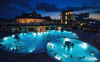 Chocholow Thermal Pools at night with visitors swimming, illuminated by blue lights.