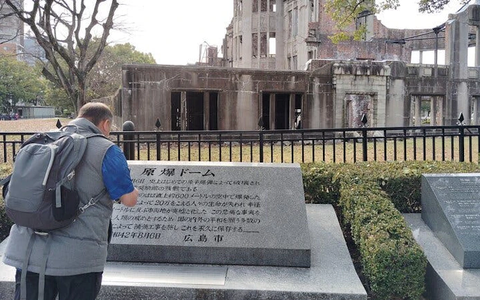 Visitor reading plaque at Hiroshima Atomic Bomb Dome, part of Peace Memorial Museum tour.