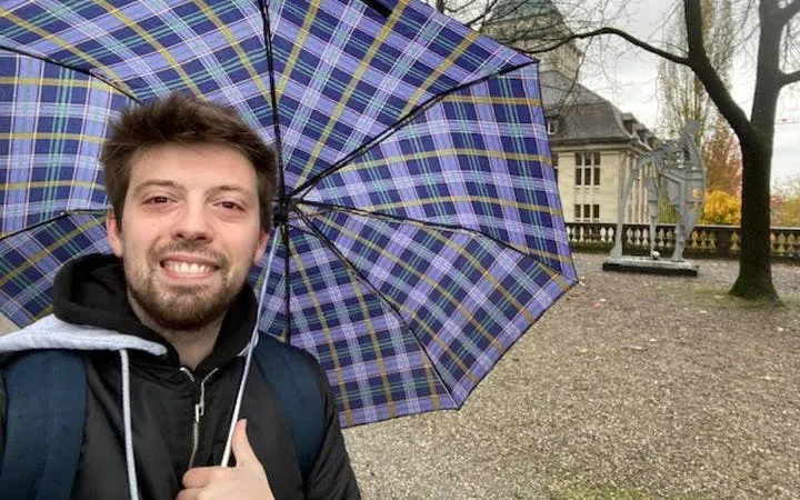 Man with umbrella near Einstein statue in Zurich during self-guided city exploration game.