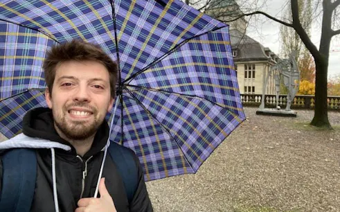Man with umbrella near Einstein statue in Zurich during self-guided city exploration game.