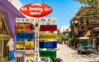 Tour booking sign on Holbox Island street, offering activities like whale shark tours and kayaking.