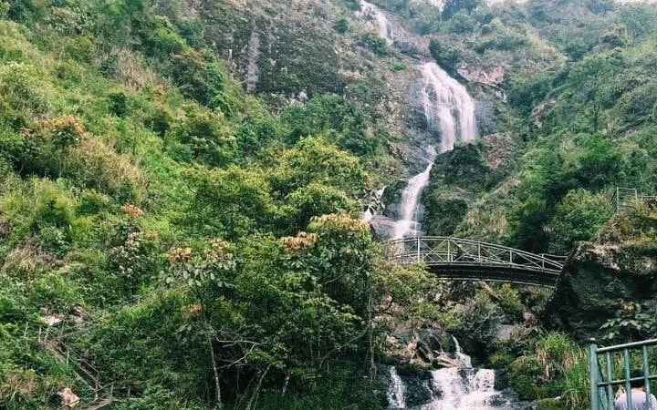 Silver Waterfall cascading down lush green hills with a bridge in Sapa, Vietnam.