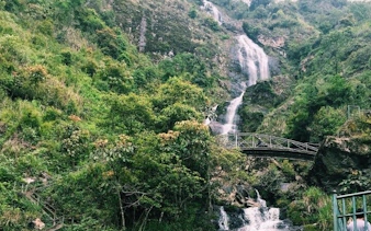 Silver Waterfall cascading down lush green hills with a bridge in Sapa, Vietnam.