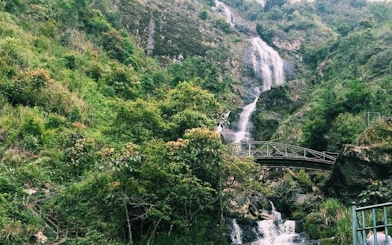 Silver Waterfall cascading down lush green hills with a bridge in Sapa, Vietnam.
