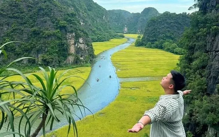 Person enjoying view of Tam Coc river and rice fields in Ninh Binh, Vietnam.