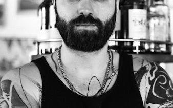 Man with tattoos and beard at Reykjavik Punk Museum bar.