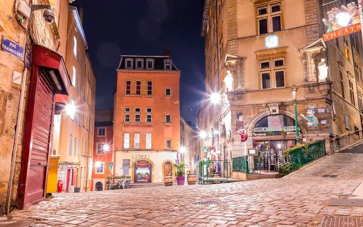 Cobblestone street in Lyon at night, featuring historic buildings and a theater, part of a haunted city exploration game.