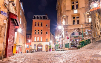 Cobblestone street in Lyon at night, featuring historic buildings and a theater, part of a haunted city exploration game.