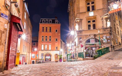 Cobblestone street in Lyon at night, featuring historic buildings and a theater, part of a haunted city exploration game.