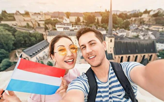 Tourists holding Luxembourg flag with cityscape view of Luxembourg City in the background.