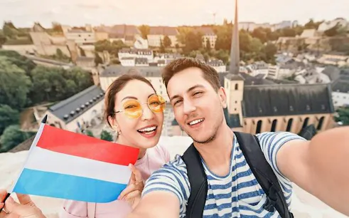Tourists holding Luxembourg flag with cityscape view of Luxembourg City in the background.