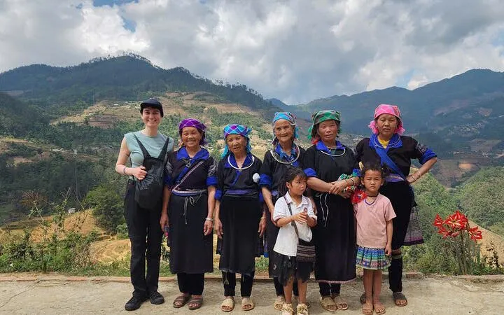 Local villagers and a tourist in traditional attire with terraced rice fields in Mu Cang Chai, Vietnam.