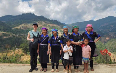 Local villagers and a tourist in traditional attire with terraced rice fields in Mu Cang Chai, Vietnam.