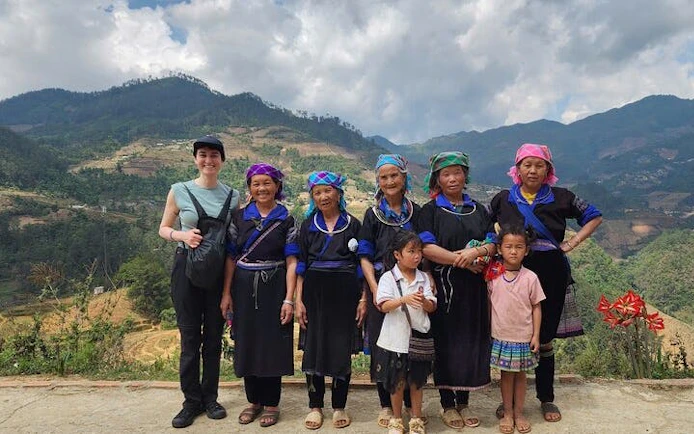 Local villagers and a tourist in traditional attire with terraced rice fields in Mu Cang Chai, Vietnam.