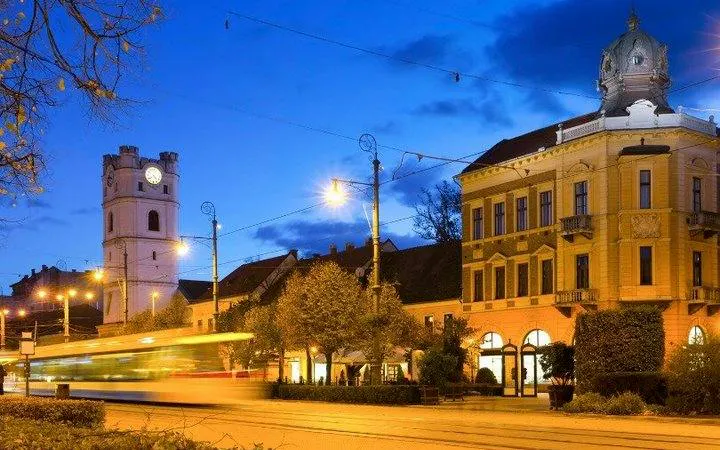 Debrecen cityscape with illuminated buildings and tram at dusk.