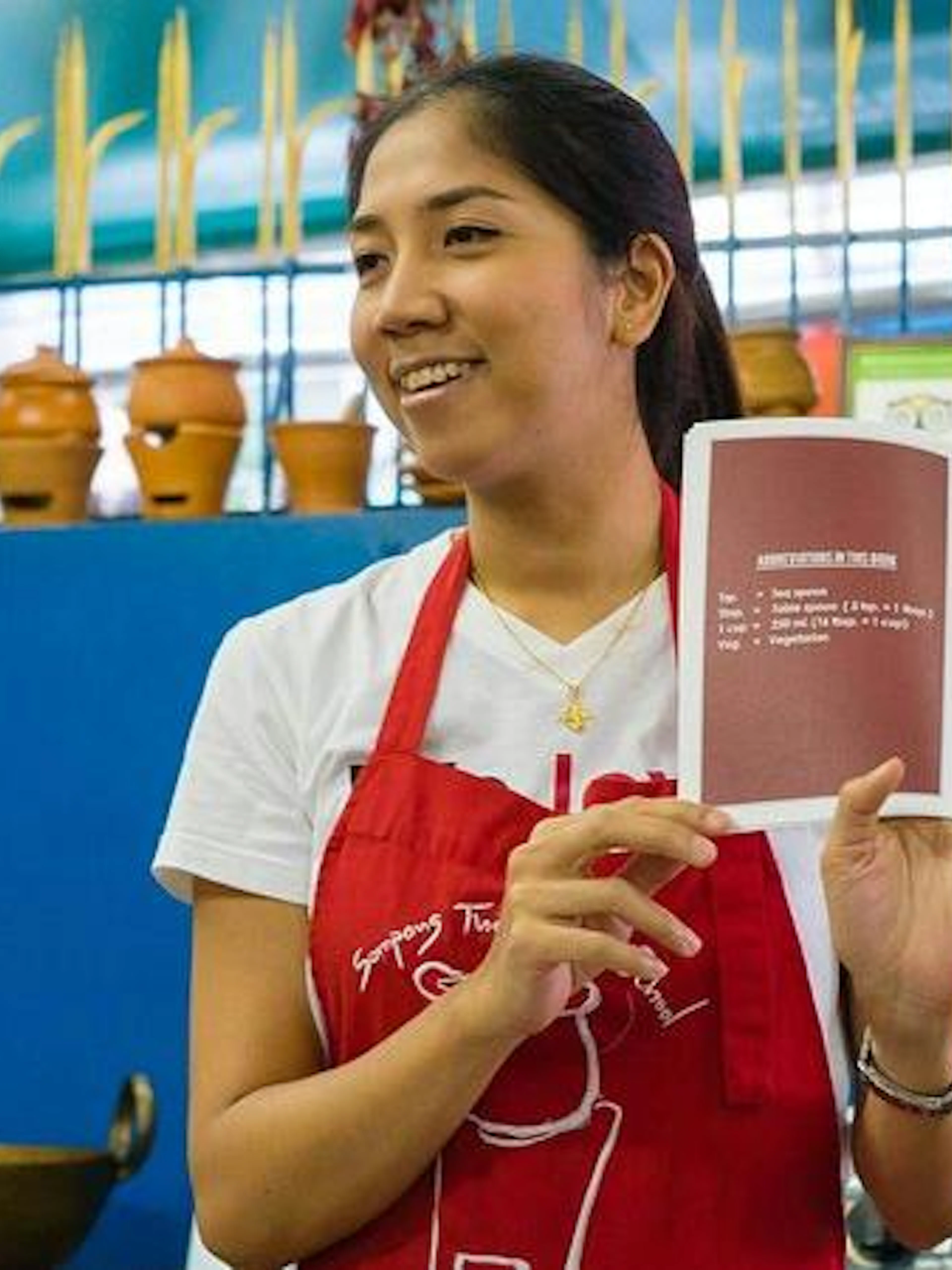 Instructor holding a recipe book at Sompong Thai Cooking School, Bangkok.