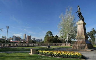 Statue in Adelaide park with city skyline in background, part of self-guided audio tour.