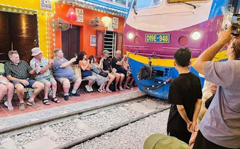 Tourists seated near passing train on Hanoi Train Street during Old Quarter cyclo tour.