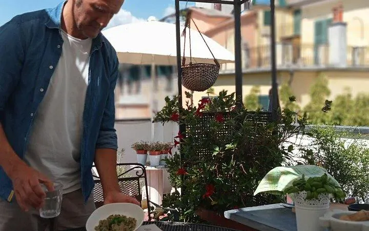 Man preparing pesto pasta on a Genoa rooftop during a cooking class with wine.