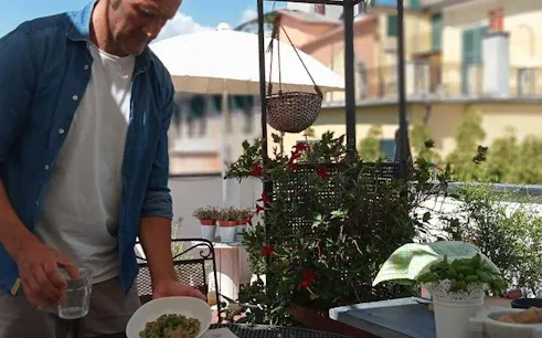 Man preparing pesto pasta on a Genoa rooftop during a cooking class with wine.