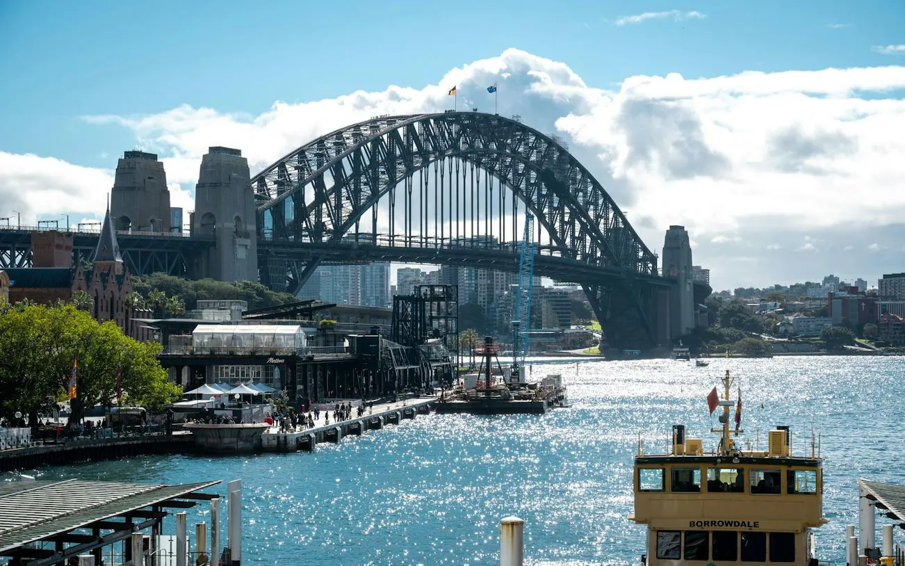 Sydney Harbour Bridge view from The Rocks, featuring a ferry on the water, part of the self-guided audio walking tour.