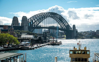 Sydney Harbour Bridge view from The Rocks, featuring a ferry on the water, part of the self-guided audio walking tour.