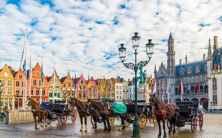 Horse-drawn carriages in Bruges' Markt Square with historical buildings in the background.