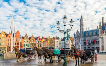 Horse-drawn carriages in Bruges' Markt Square with historical buildings in the background.