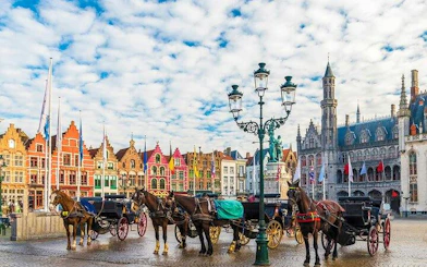 Horse-drawn carriages in Bruges' Markt Square with historical buildings in the background.