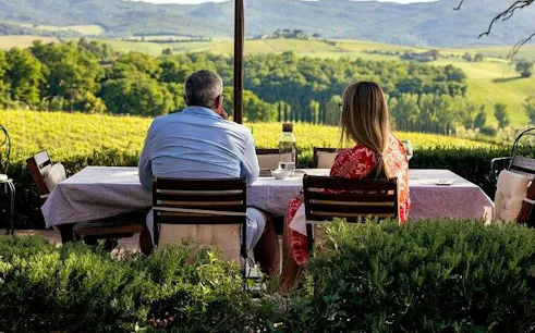 Couple enjoying wine at a table overlooking Montalcino vineyards during a guided tour.