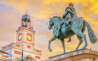 Equestrian statue and clock tower at Puerta del Sol, Madrid, during sunset.