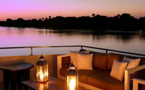 Sunset view from a boat on the Zambezi River, Victoria Falls, with lantern-lit seating.
