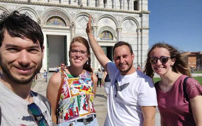 Group of tourists enjoying a self-guided exploration game in front of Pisa Cathedral, Italy.