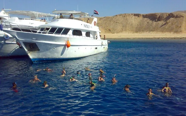 Snorkelers near a boat at Tiran Island, Sharm El Sheikh, with desert landscape in the background.