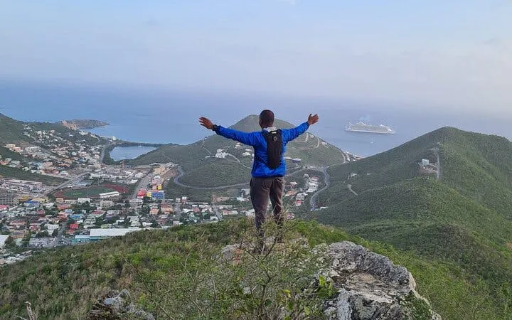 Hiker on St. Maarten's highest point overlooking cityscape and ocean with cruise ship.