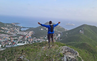 Hiker on St. Maarten's highest point overlooking cityscape and ocean with cruise ship.