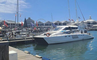 Catamaran docked at Cape Town harbor with waterfront buildings and Ferris wheel in the background.