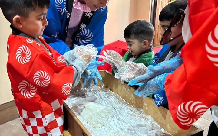Children participating in a traditional mochi pounding experience, wearing cultural costumes.